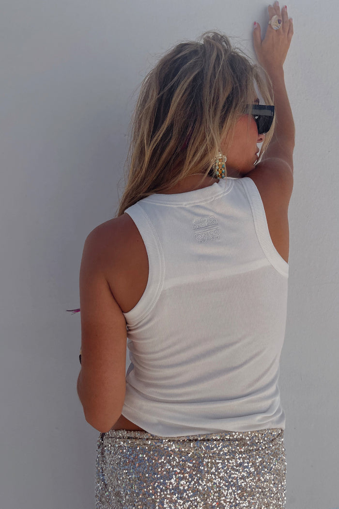 White Ribbed Tank with an embroidered logo detail, shown from behind on a model wearing sequin bottoms.